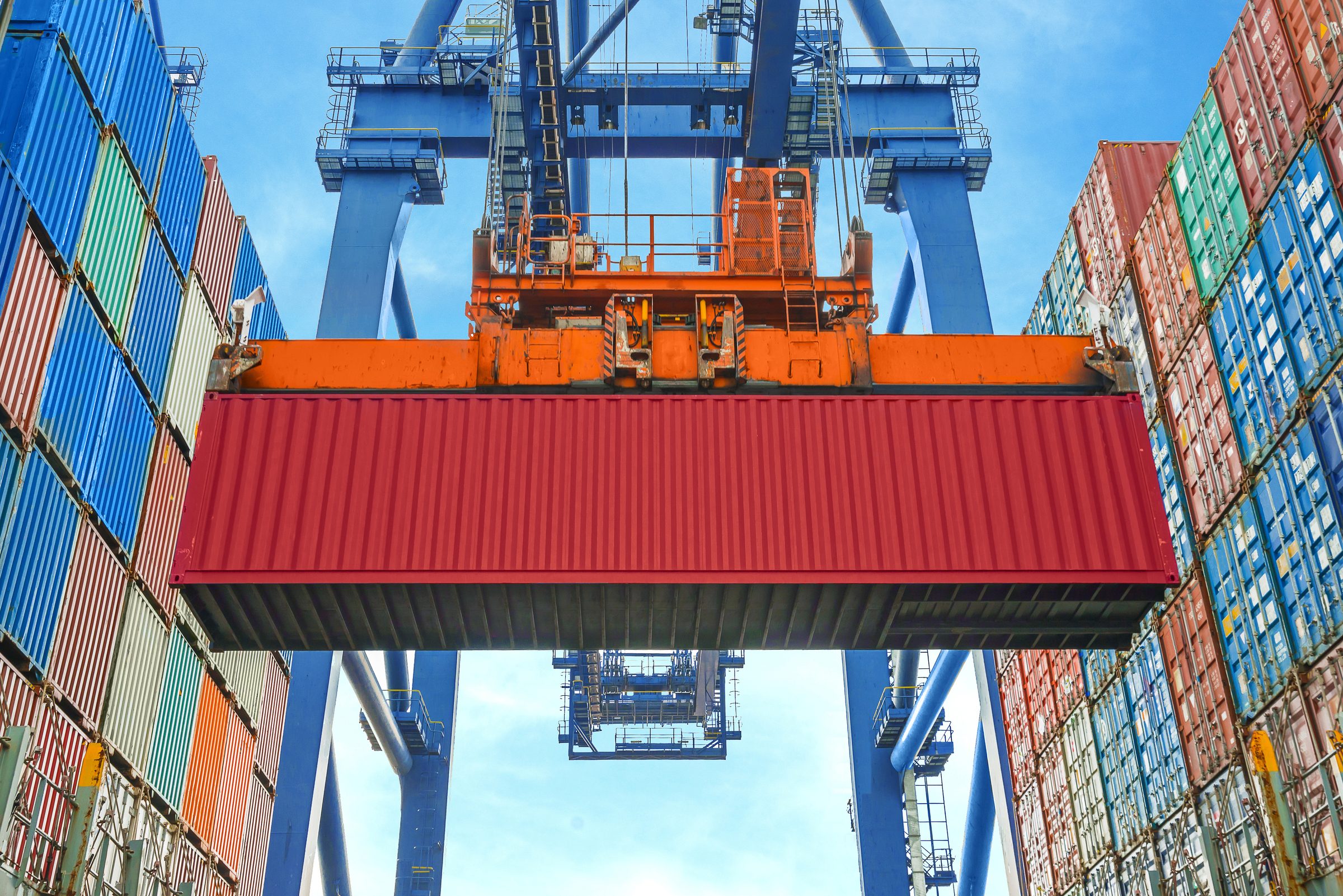 Gantry crane lifting a shipping container between stacked containers