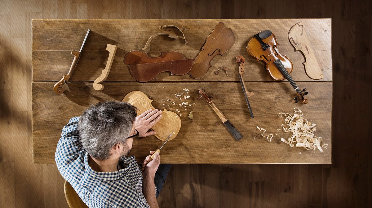Craftsman shaping a violin at a workbench, seen from above